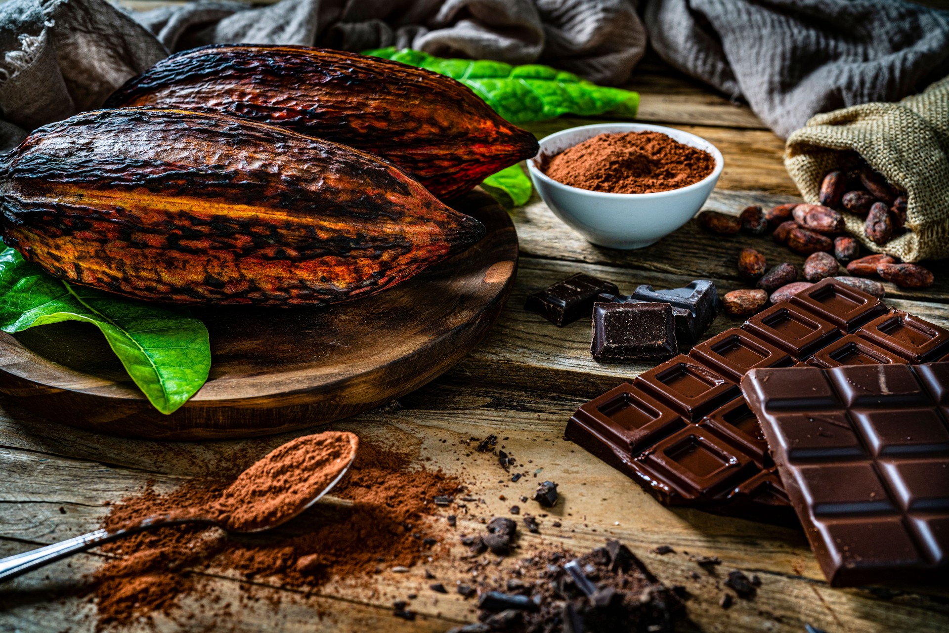 Dark chocolate bars, cocoa pods and cocoa powder on rustic wooden table.